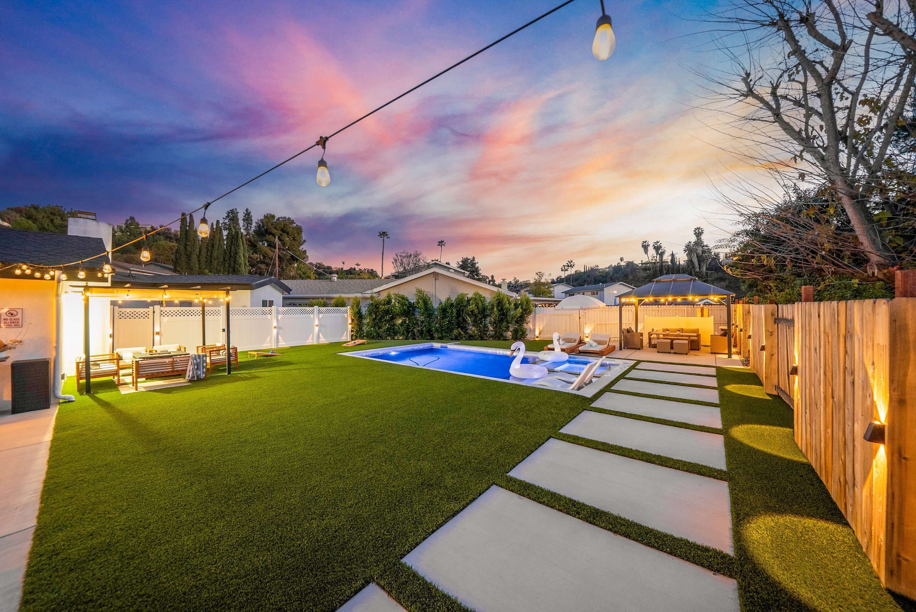 A backyard with a swimming pool, artificial grass, and a wooden deck.