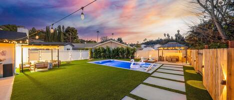 A backyard with a swimming pool, artificial grass, and a wooden deck.