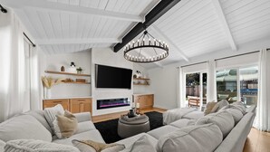 Ein modernes Wohnzimmer mit einer großen Eckcouch, einem Kamin, einem Fernseher und einer Kristallleuchter.