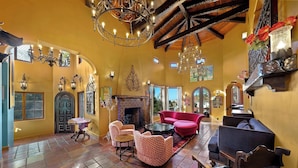 Un salón amplio con chimenea, muebles rojos y rosados, y una araña.