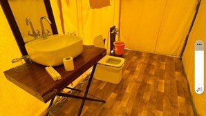 Une pièce compacte aux murs d’une teinte jaune, dotée d’un plancher en bois, d’un lavabo, d’un miroir, d’une petite table, d’une chaise et de toilettes portables.