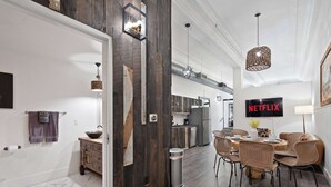 Cozinha moderna com detalhes em madeira escura, sala de jantar com cadeiras de vime e um letreiro da Netflix na parede.