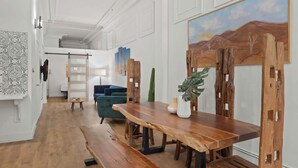 A spacious room with a wooden dining table, a blue sofa, and a large painting on the wall. - Woolworth Loft – Gaslamp 4BR Downtown Pad w/ Tub (San Diego)