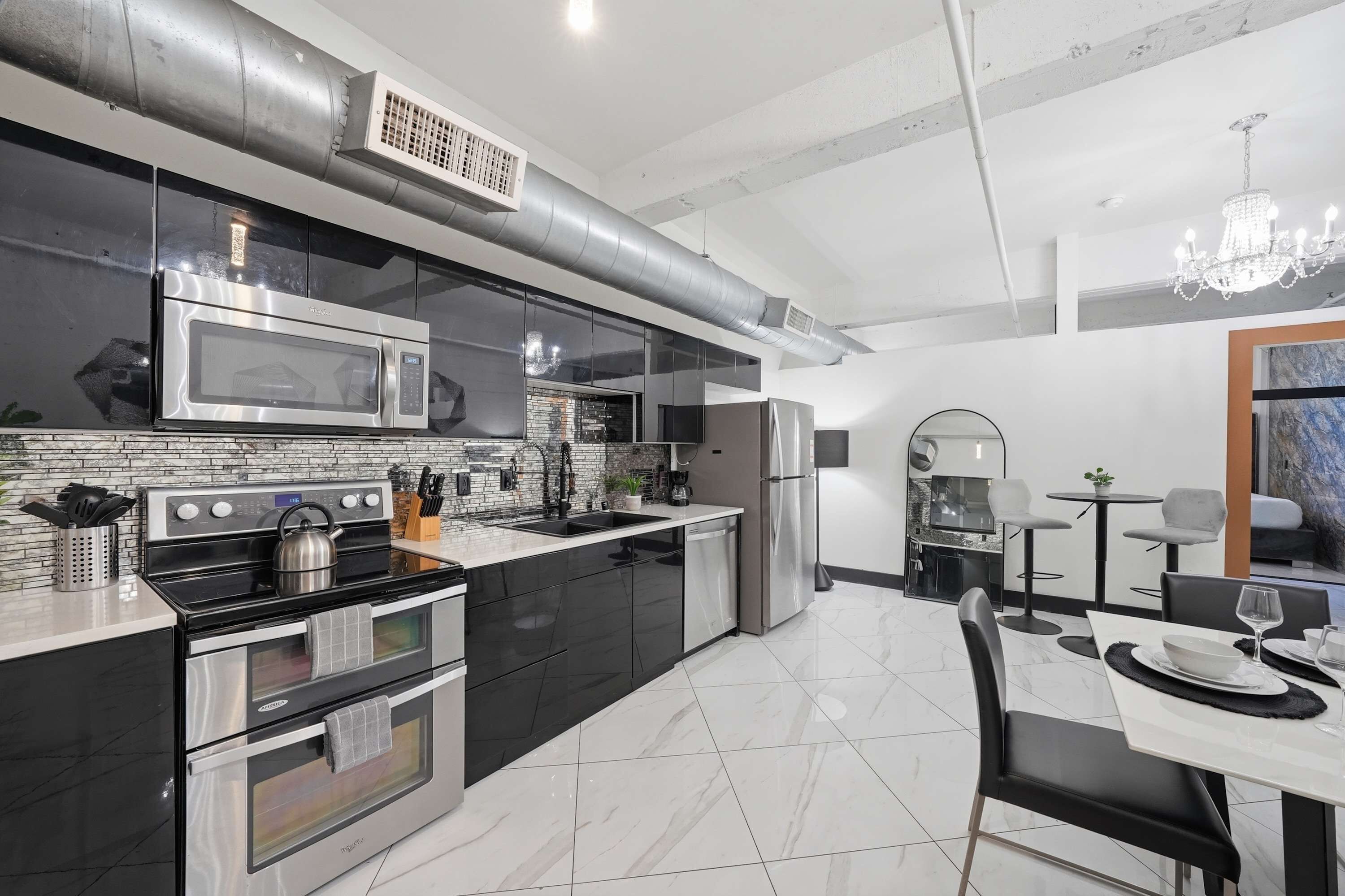 A modern kitchen with stainless steel appliances, a dining area with a table and chairs, and a chandelier.