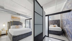 A modern bedroom with a large bed, a bedside table, and a wall-mounted artwork. - Woolworth Loft – Elegant Stay w/ City Views (San Diego)
