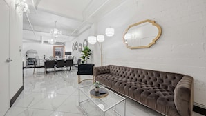 A modern living room with a tufted sofa, a glass coffee table, and a dining area in the background. - Woolworth Loft – Elegant Stay w/ City Views (San Diego)