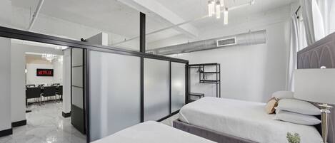 Habitación de hotel moderna con dos camas, un escritorio, una silla, una planta pequeña y vistas a un comedor.