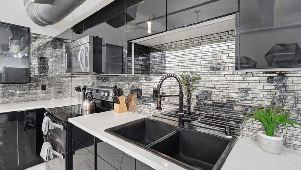 A modern kitchen with a double sink, stainless steel appliances, and a brick backsplash. - Woolworth Loft – Elegant Stay w/ City Views (San Diego)