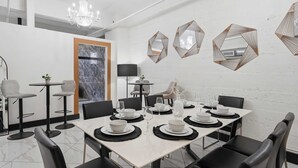 A modern dining area with a white table set for six, black chairs, and geometric wall mirrors. - Woolworth Loft – Elegant Stay w/ City Views (San Diego)