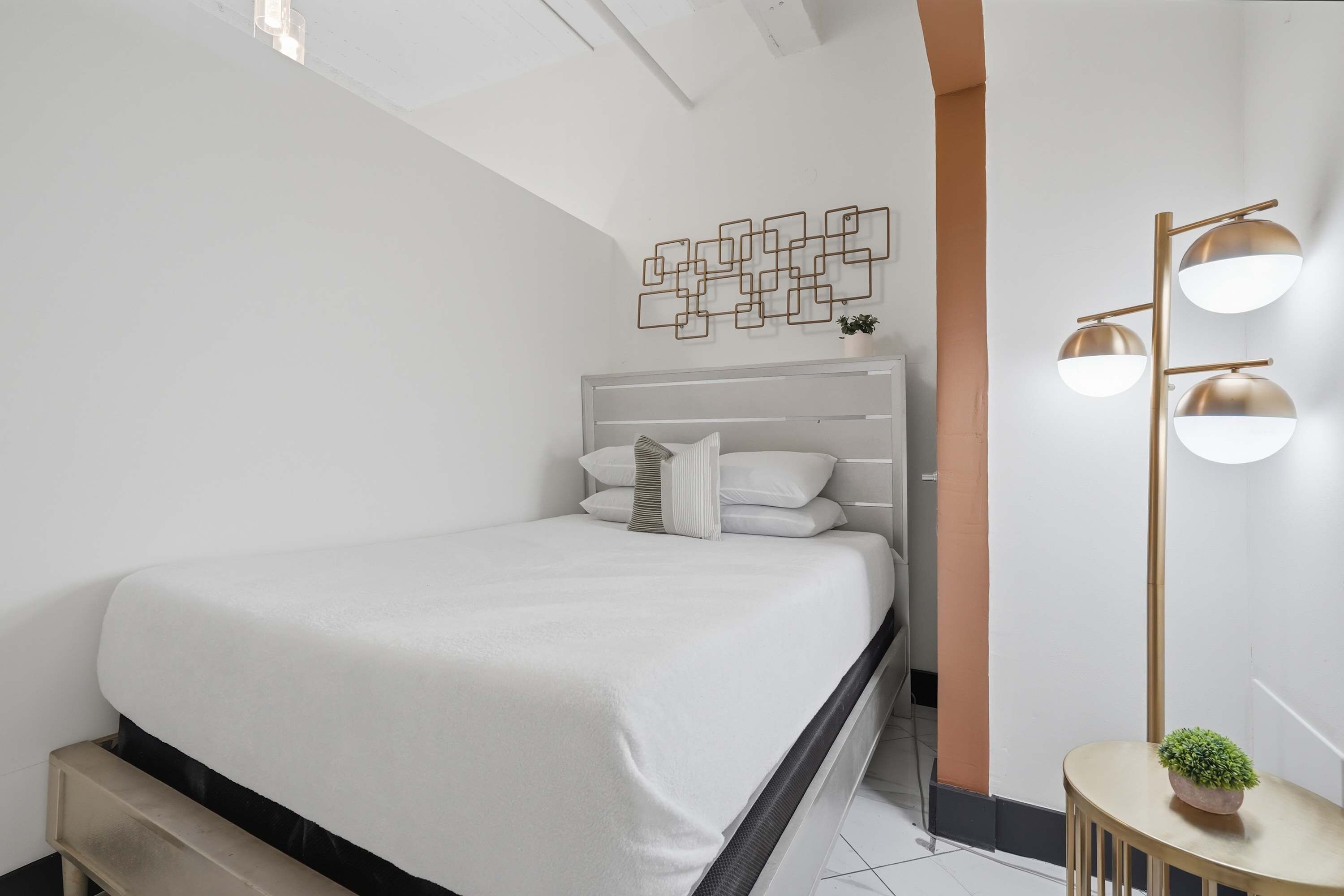 A modern bedroom with a bed, a bedside table with a plant, and a wall-mounted light fixture.