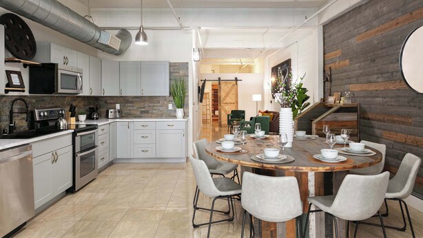 Una cocina moderna con armarios blancos, electrodomésticos de acero inoxidable y una mesa de comedor de madera dispuesta para seis comensales.