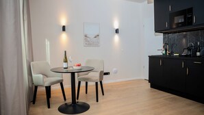 A modern kitchen with black cabinets, a round dining table with two chairs, and a wine bottle on the table. - The MYDE Hamburg Serviced Apartments (Hamburg)
