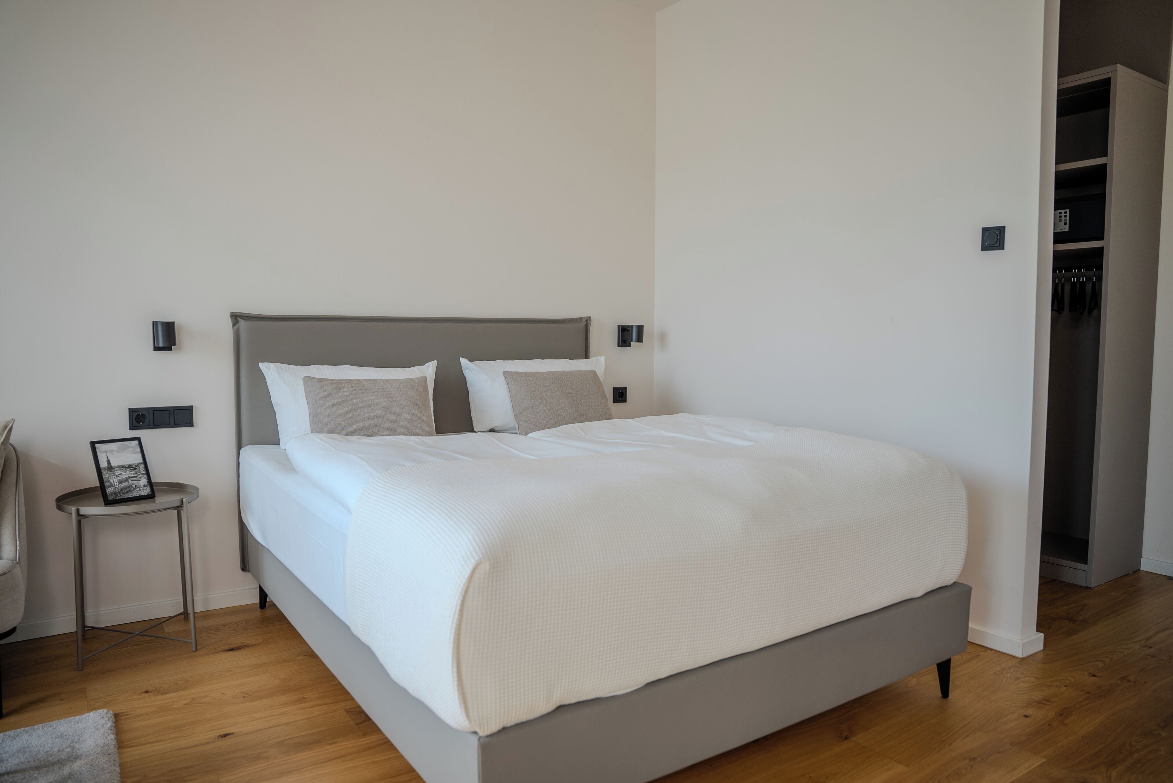 Ein modernes Schlafzimmer mit einem großen Bett, einem Nachttisch mit Bilderrahmen und einem Kleiderschrank.