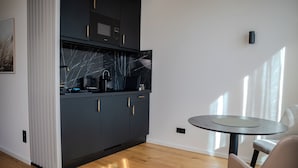 A modern kitchen with dark cabinetry, a marble backsplash, and a round table with a chair. - The MYDE Hamburg Serviced Apartments (Hamburg)