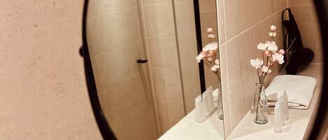 Un baño con espejo, ducha y lavabo con un florero.