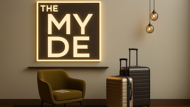 A modern room with a large illuminated sign on the wall, a single armchair, and two pieces of luggage. - The MYDE Hamburg Serviced Apartments (Hamburg)