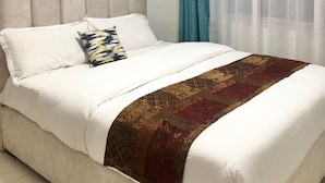 A bed with a beige headboard, white bedding, and a decorative throw. - Kiambu Zone Heights (Nairobi)