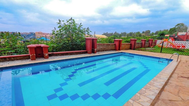 A rectangular swimming pool with blue tiles and a stone border, surrounded by a low stone wall and red planters. - Kiambu Zone Heights (Nairobi)