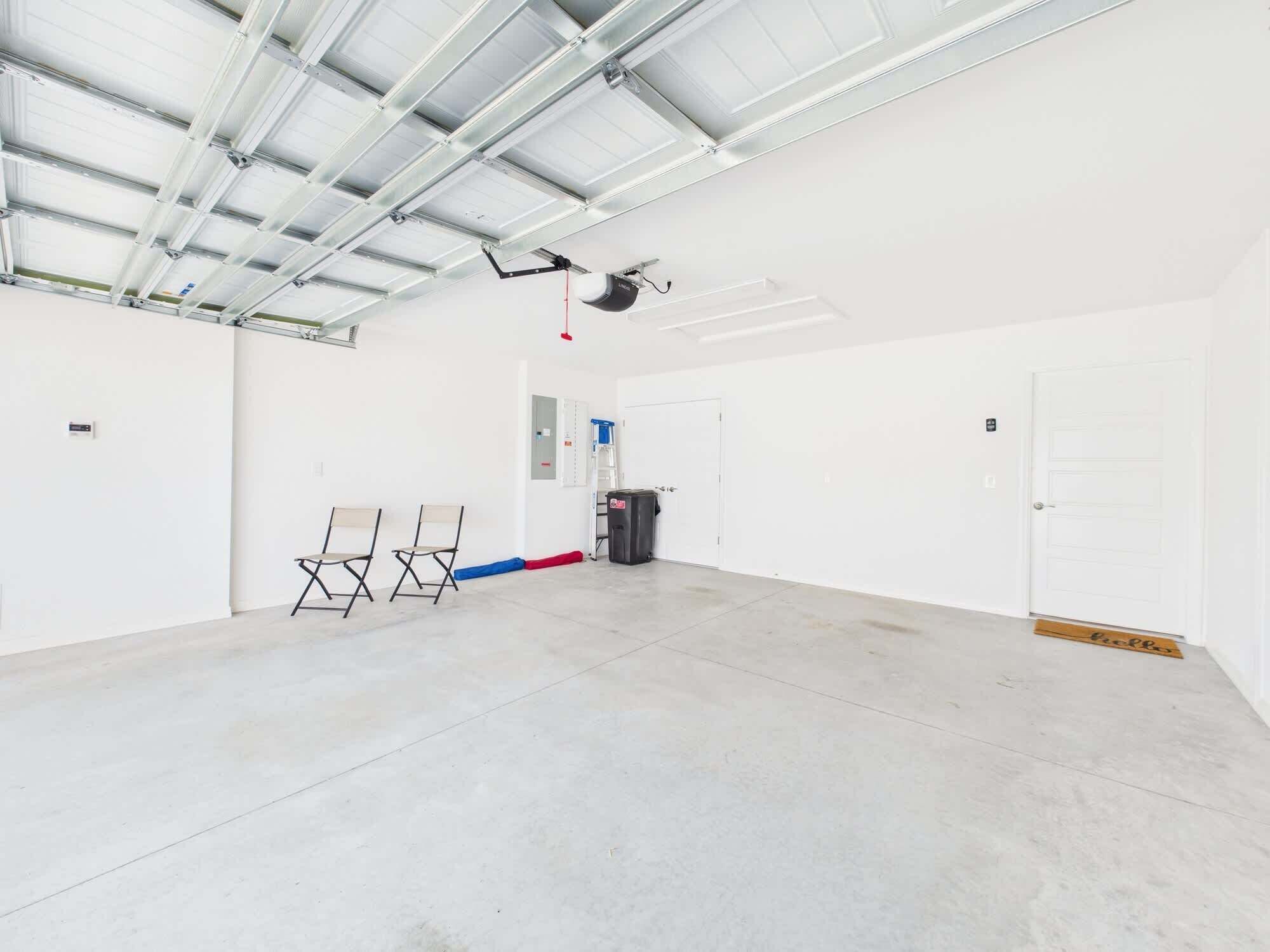 Il s’agit d’une pièce spacieuse, bien éclairée et de style industriel, avec un plafond haut, des murs blancs et un sol en béton. Contre le mur, on trouve trois chaises pliantes, une échelle et une poubelle.