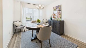 A dining area with a round table, chairs, a chandelier, a cabinet, and a window with curtains. - Near Sawgrass Grove in The Village of Newell (The Villages)
