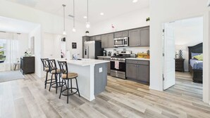A modern kitchen with a central island, grey cabinets, stainless steel appliances, and pendant lighting. - Near Sawgrass Grove in The Village of Newell (The Villages)