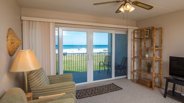 Un salon comprenant un canapé, une lampe, un téléviseur, une bibliothèque et un balcon avec vue sur la plage.