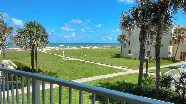 A balcony with a view of a well-maintained lawn, palm trees, and a distant beach. - Pier Point South Ocean View Condos B-15 (St. Augustine)