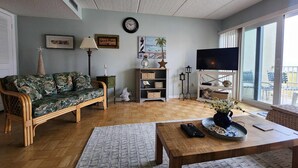 A living room with a sofa, a coffee table, a TV, and a bookshelf. - Pier Point South Ocean View Condos B-15 (St. Augustine)