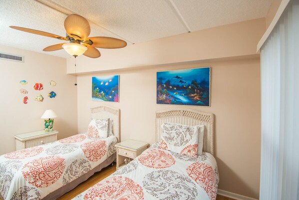 A bedroom with two beds, a ceiling fan, and two wall-mounted paintings.