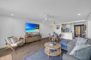 Uma sala de estar moderna com um sofá, mesa de centro e uma TV exibindo uma cena de praia.