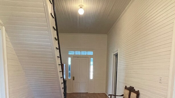 A hallway with wooden flooring, a chair, a basket of items, and a door at the end. - “Down Home” - Charming Antebellum Farm House (Edgefield)