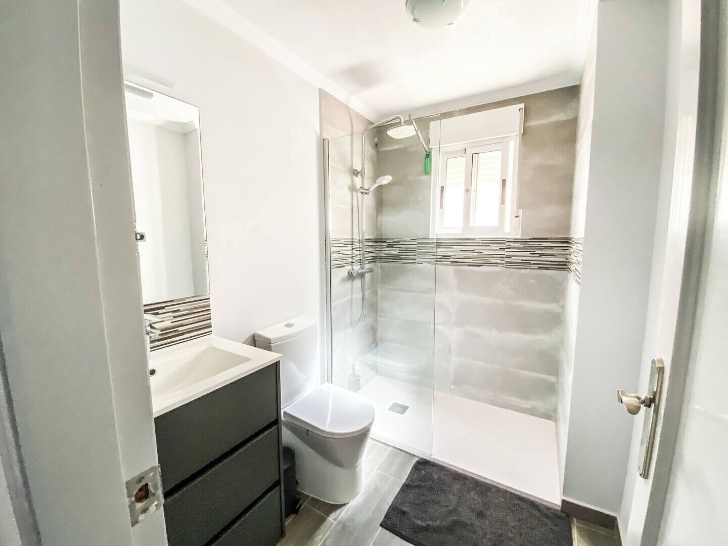 A modern bathroom with a glass shower enclosure, a white sink, and a dark-toned vanity.