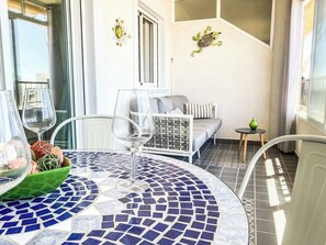 Una habitación soleada con suelo de baldosas, una mesa redonda con un vaso y un sofá con cojines.
