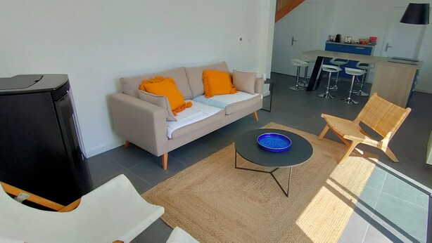 Een moderne woonkamer met een bank, salontafel en televisie. Achterin is een keuken met barkrukken en een eettafel.