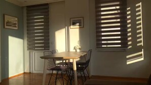 A dining area with a wooden table and metal chairs, two framed pictures on the wall, and a window with blinds. - 2-bedroom apartment in fabulous Alanya with WiFi, AC (Antalya)