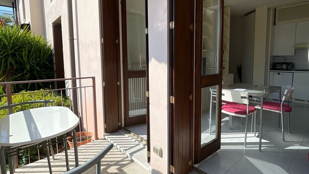 A balcony with a table and chairs, a sliding glass door leading to a kitchen area with a dining table and chairs. - 3V Apartments UGO WITH POOL (Bardolino)