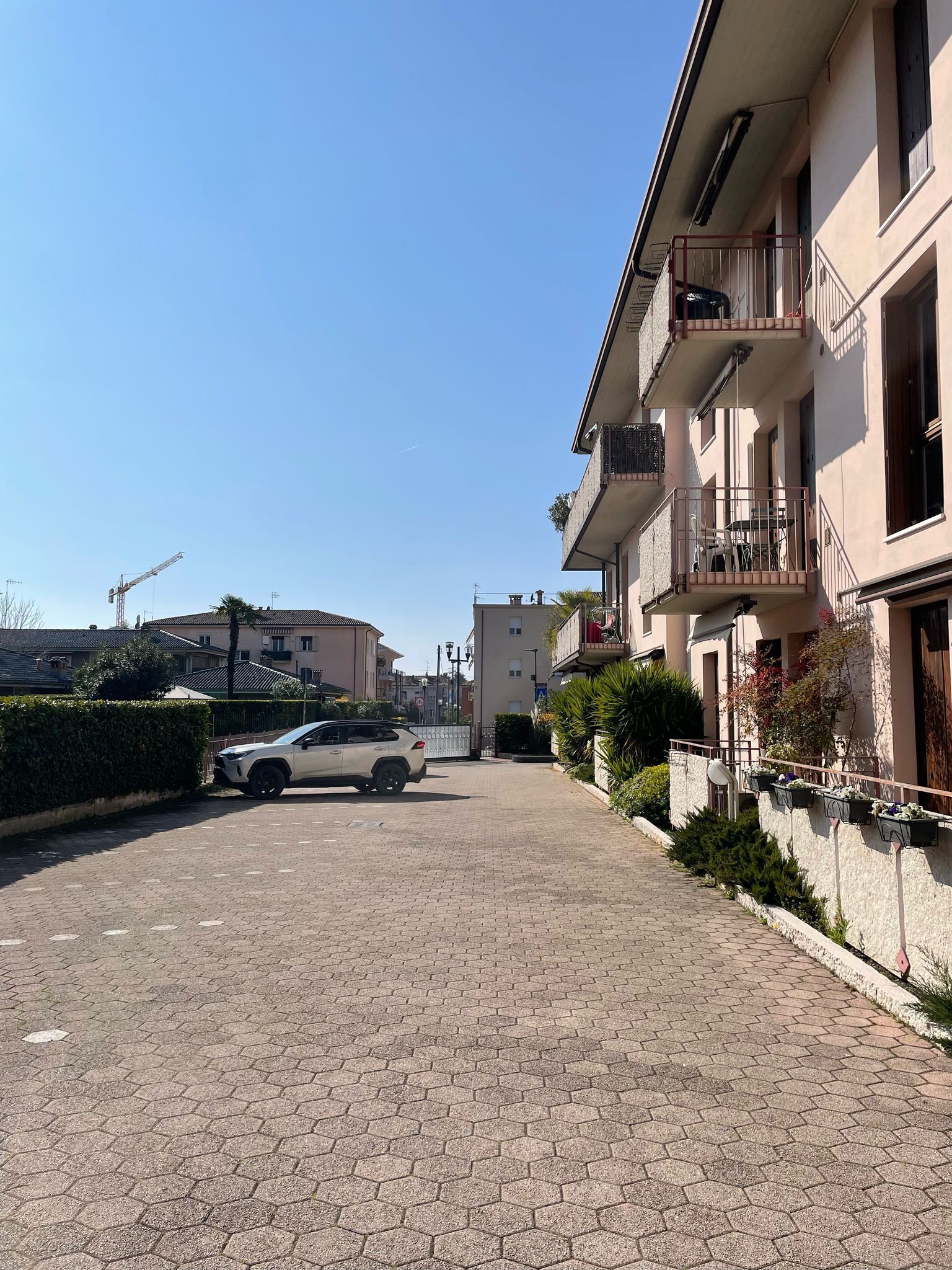A paved driveway leading to a residential building with balconies, a parked car, and a construction crane in the background.