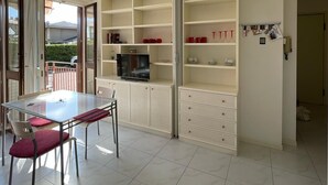 A modern kitchen with a dining area, featuring a glass table, chairs, and a TV on a cabinet. - 3V Apartments UGO WITH POOL (Bardolino)