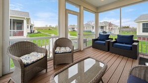 A covered outdoor area with wicker furniture and glass tables, overlooking a residential neighborhood.