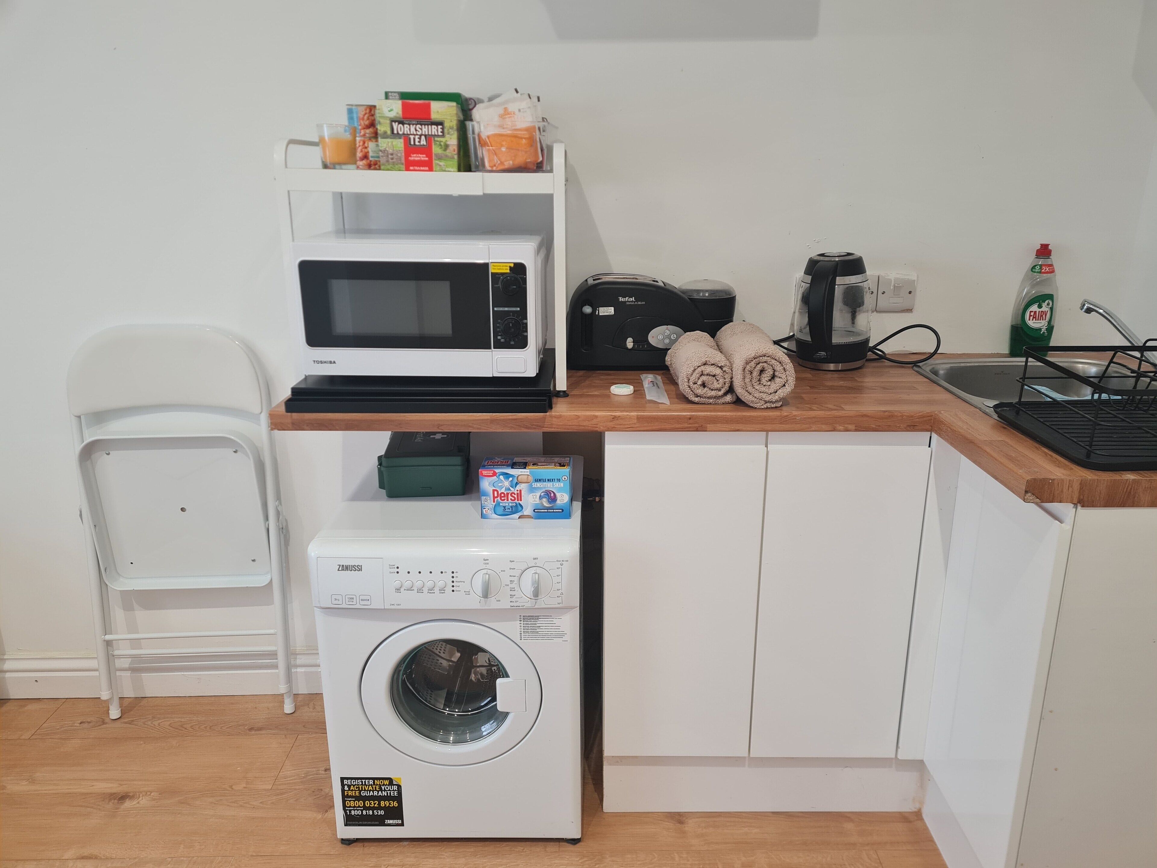 Eine kleine Küchenzeile mit Mikrowelle, Toaster, Wasserkocher und Waschmaschine.
