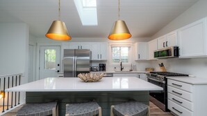 A modern kitchen with white cabinets, stainless steel appliances, and a large island with bar stools. - New Buffalo With Hot Tub and Association Beach! (New Buffalo)
