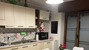 A modern kitchen with white cabinets, a black microwave, and a dining table with white chairs. - Superior Apartment to Pompeii (Boscoreale)