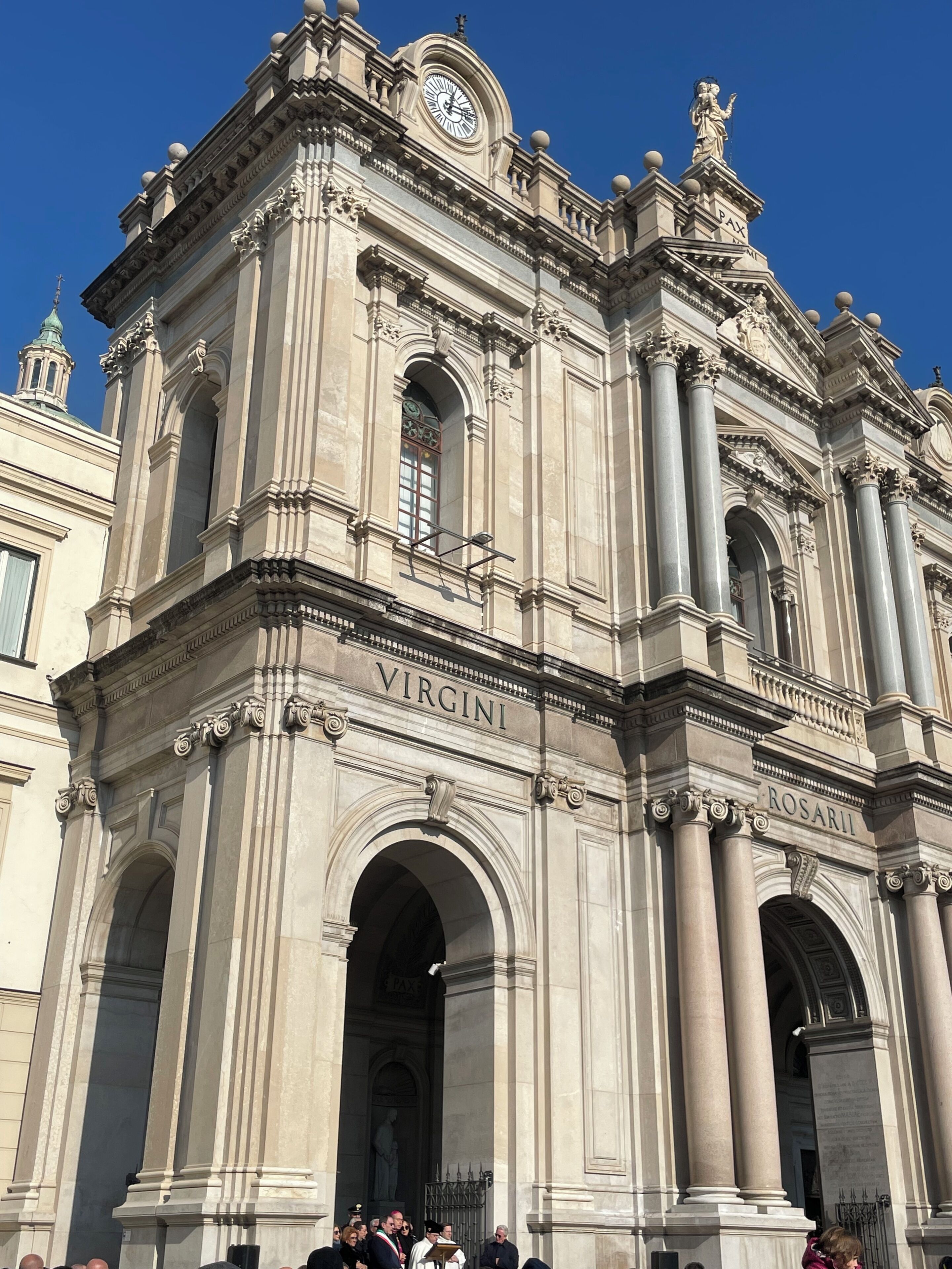 A grand historical building with the name 'VIRGINI' and 'ROSARII' inscribed on its facade, featuring classical architectural elements like columns and arches.