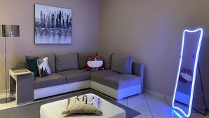 A modern living room with a grey sectional sofa, a standing mirror, and a framed cityscape artwork on the wall. - Superior Apartment to Pompeii (Boscoreale)