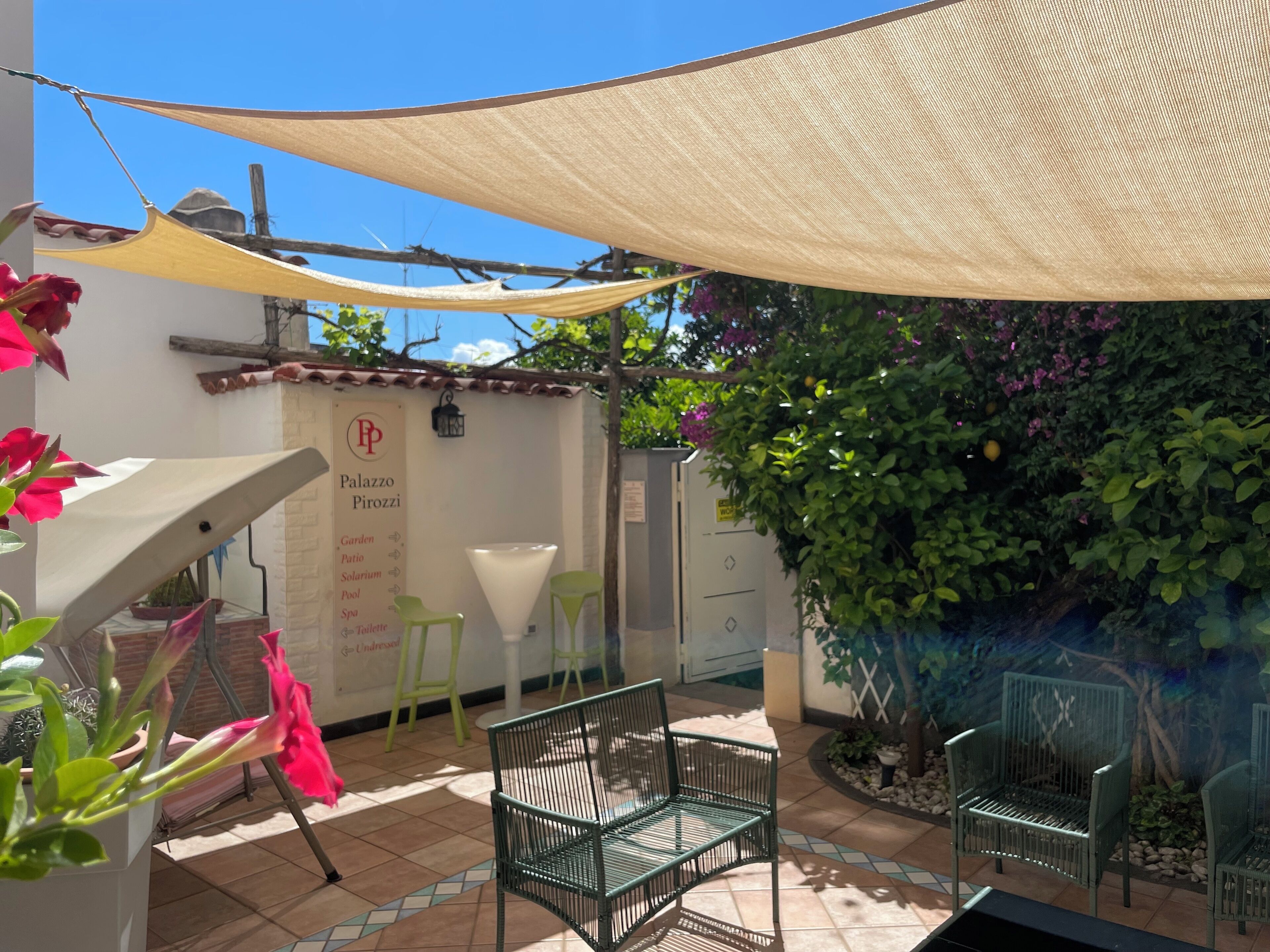 A patio area with outdoor seating, a shaded area, and a wall with greenery.