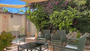An outdoor patio area with green metal chairs and a black table, surrounded by lush greenery and purple flowers. - Superior Apartment to Pompeii (Boscoreale)