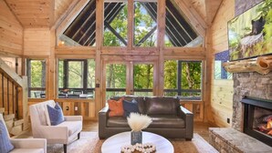 A spacious living room with a high ceiling, large windows, a stone fireplace, and a cozy seating area.