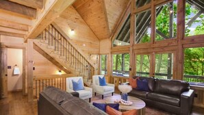 A spacious living area with a staircase, wooden walls, and large windows offering a view of the outdoors.