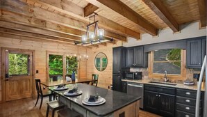 A wooden interior with a kitchen island, wooden ceiling beams, and large windows.
