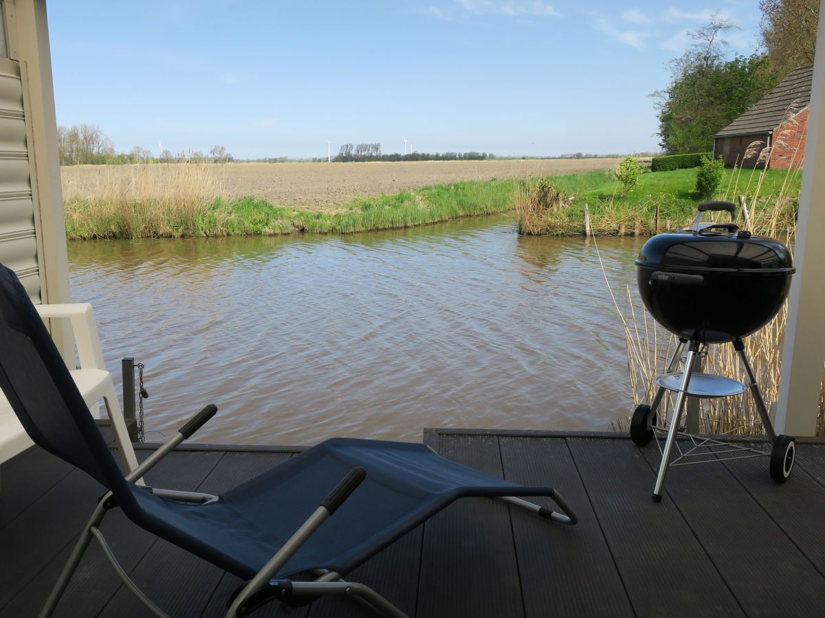 A deck with a chair and a grill, overlooking a water body and fields.